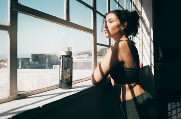 Window, fitness and relax with a sports woman looking at the view during a break in the gym for...