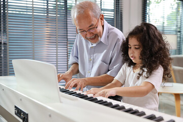 Happy smiling asian senior man sitting and playing piano while teaching grandchild in living room...