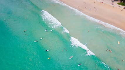 Aerial drone view of a group of surfers riding wave on surfboard at Kata Beach in Phuket, Thailand....