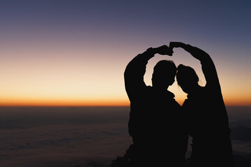 Silhouette  of the romantic scene of the couple sitting on the hill at sunset time. young couple...