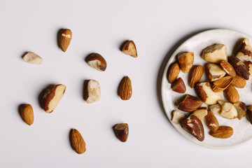 top view scattered almonds and Brazil nuts detail on a plate and white background