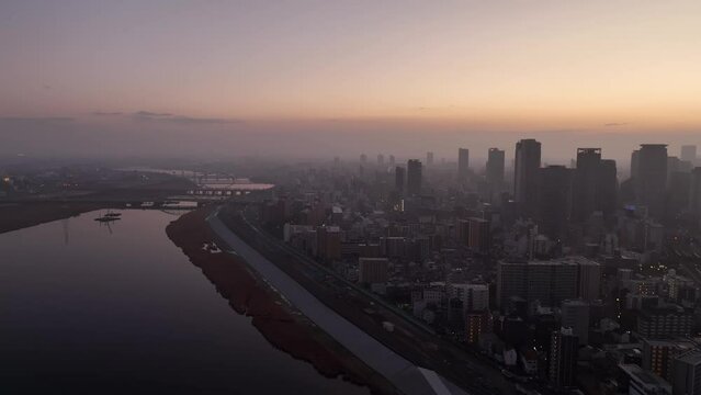 Aerial view of wide river and sprawling modern city in haze at sunrise