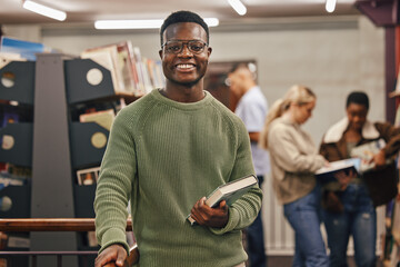 Black man, book and portrait in library with smile, research and studying at college for education. African gen z student, happy and university for books, learning or vision for future career goal - obrazy, fototapety, plakaty