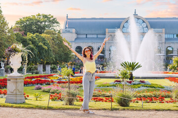 Fototapeta na wymiar Happy tourist girl walks and enjoys holiday in the Botanical Flora garden in Cologne, Germany. Majestic fountain in the background