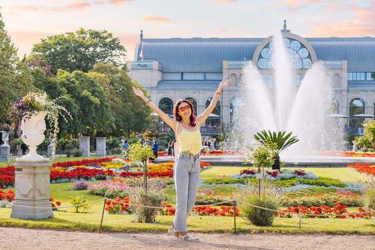 Happy tourist girl walks and enjoys holiday in the Botanical Flora garden in Cologne, Germany. Majestic fountain in the background