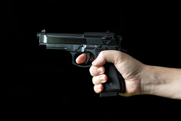 Hand holding a gun, on black background. concept of the crime of banditry. A dangerous shooter and...