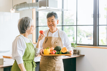 家のキッチンの前で笑顔で話すアジア人高齢者夫婦（料理教室）

