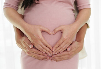 pregnant couple making hand heart gesture on belly