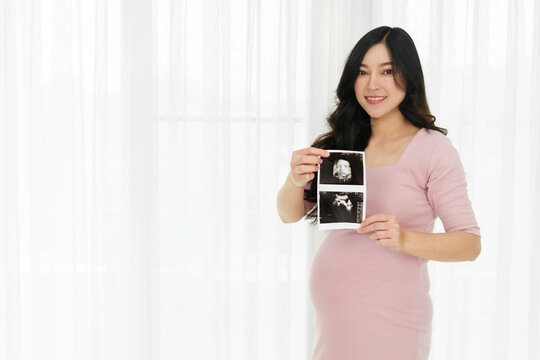 happy pregnant woman showing ultrasound photo of baby on window background