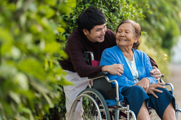 happy young man (grandson) embracing with senior woman in wheelchair at park