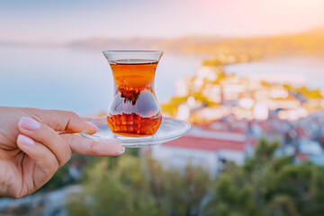 Fototapeta Delicious and fragrant Turkish tea in a traditional authentic bardak glass in the hand of a tourist against the backdrop of a resort town obraz