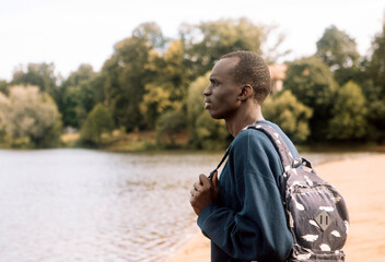 A young black man in sportswear with a backpack walks near the lake.