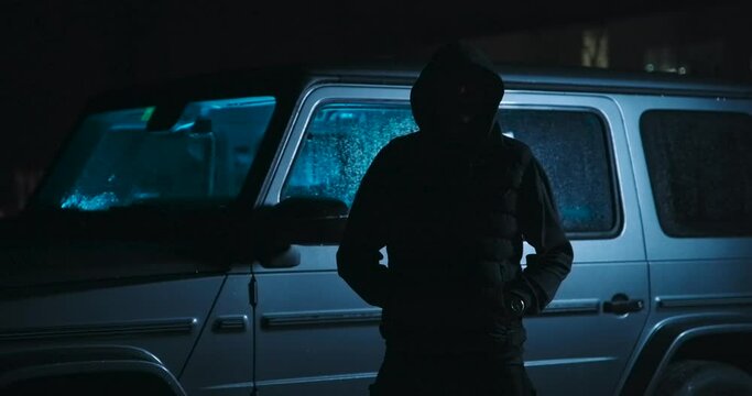 Dark man in front of a car at night.