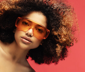 Young woman wearing sunglasses isolated on studio red background. Excited african american female.