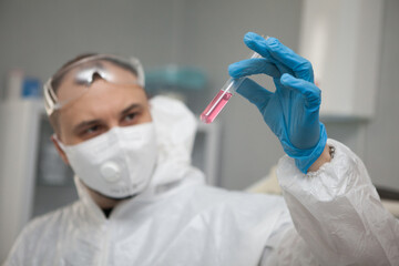 Scientific virologist. Biologist in protective suit and blue gloves holds test tube. Test tube with viruses concept. Medicine and antidote in doctor hands. Virus University employee.