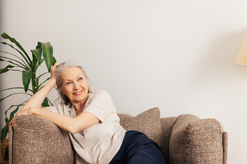 Pensive senior woman relaxing at home sitting in an armchair