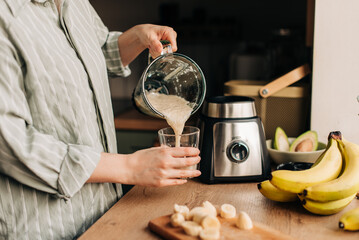 A Woman Prepares A Detox Cocktail At Home. A woman pours a banana smoothie into a glass. the concept of healthy eating