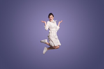 Full length photo of millennial woman wearing dress jump shrugging shoulders isolated on purple...