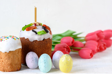 Painted Easter eggs, tulips and cakes on white wooden table