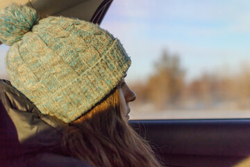 Close-up of a young woman in a knitted hat and jacket in a bad mood sits in a car looks out the window with sadness and despair, ready to cry at any moment, copy space.