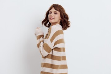 a sweet, pleasant woman with a short haircut stands on a light background in a stylish beige, striped sweater and standing sideways smiles affably at the camera