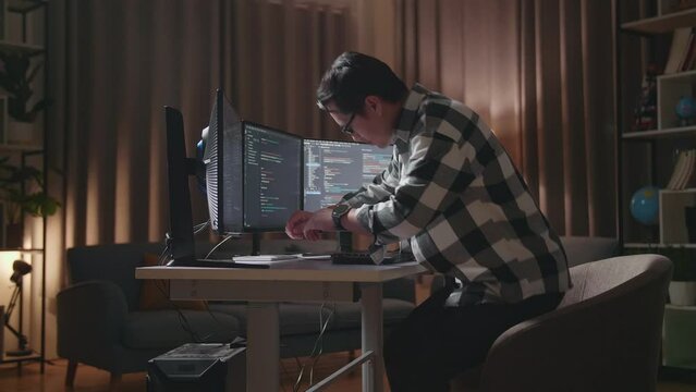 Asian Male Programmer Walking Into The Working Space Before Sitting To Creating Software Engineer Developing App, Program, Video Game On Desktop Computer At Home
