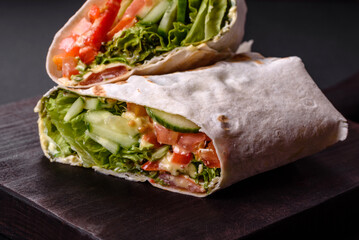 Delicious fresh shawarma with tomatoes, peppers, cucumber on a dark concrete background
