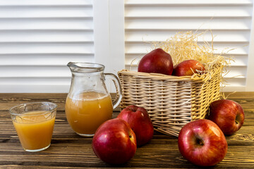 Red apples in a basket and apple juice in a jug on a wooden table