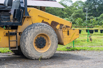 Obraz premium Side view of a yellow road roller that's on the stand by mode without the roll at a park
