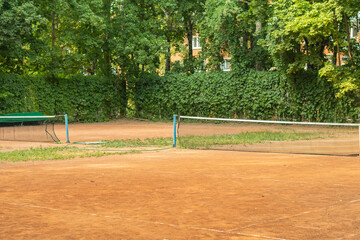 DIY amateur tennis court in a small town. A empty place for sports lovers. Fence from green bushes in climbing plants. © Николай Батаев