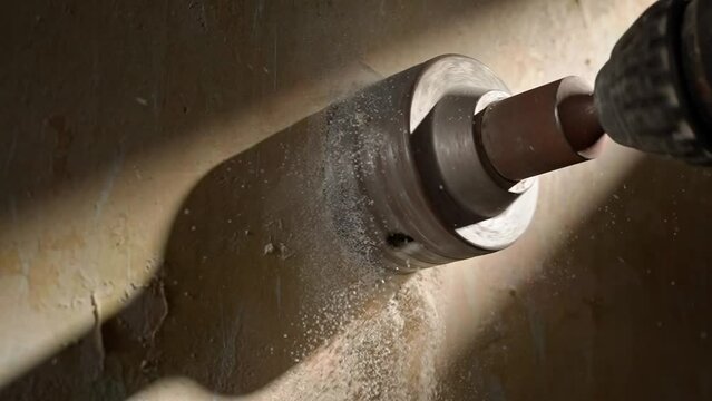 Round metal nozzle that drills a hole in the wall for socket. Perforator with a rotating nozzle crown, macro shot in beam of light. In the process of drilling wall, particles of white plaster scatter.