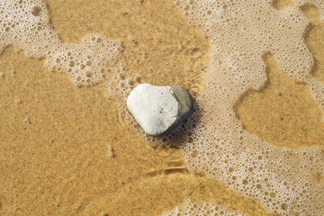 A heart-shaped stone on the shore. Sandy beach with a light sea wave. Background to a pleasant holiday, relaxing vacation and hiking in an ecologically clean area.