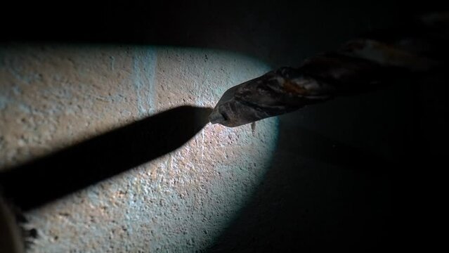 Process of drilling hole in wall using electric drill or perforator in dark with light beam. Macro shot of metal spiral auger drill is rotating. In process of drilling white dust from plaster crumbles