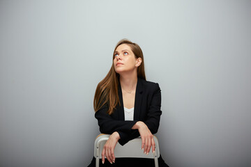 Serious woman in black suit sitting on chair and looking up.