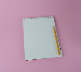 Spiral notebook with yellow pencil on a pink background in close-up.	