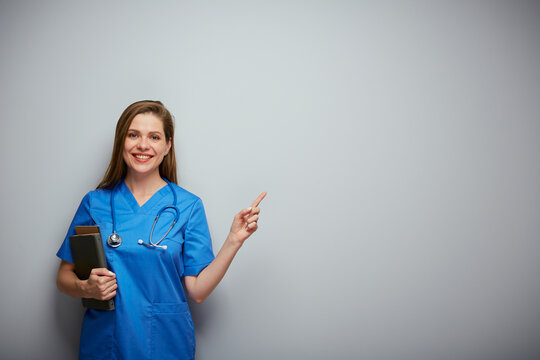Smiling student woman doctor or nurse with medical education holding book and pointing finger. Isolated portrait of female medical worker.