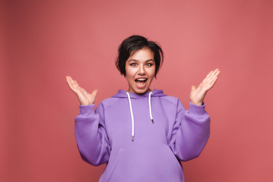 An image of an excited, screaming young woman standing isolated on a pink background. A viewing camera. studio portrait