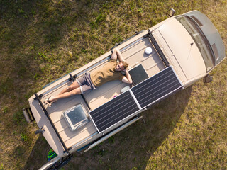 Aerial view of a man lying on the roof of a camper van - obrazy, fototapety, plakaty