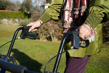 Closeup portrait of senior grandmother hands holding a walker, walking in a garden in a sunny day.