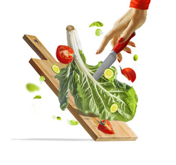 Women hand with knife making healthy salad with flying green lettuce , tomatioes and cucumber on cutting board. Isolated. Food levitation - obrazy, fototapety, plakaty