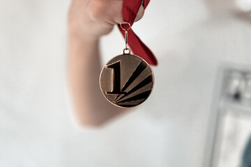 Man, boy holding a gold medal in his hand, medal with red ribbon,