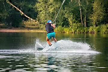 A young woman wakeboarding on a lake on summer day in a life  jacket. Soft focus. Action blur.