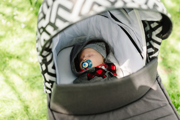 Baby boy in jacket and hat sleeping in modern stroller on a walk in a park. Child in buggy. Close...