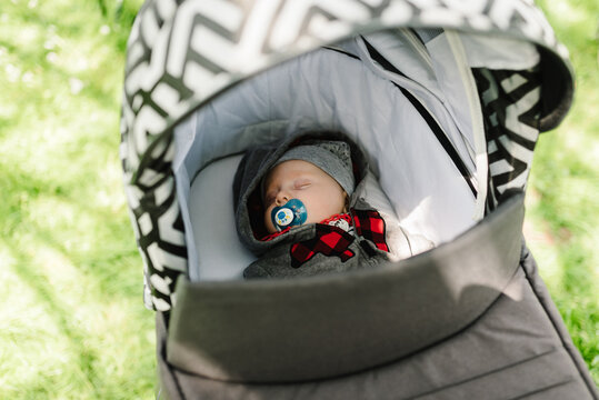 Baby boy in jacket and hat sleeping in modern stroller on a walk in a park. Child in buggy. Close Up of stroller with newborn. Top view.