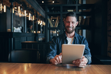 Modern hipster businessman drinking coffee in the city cafe during lunch time and working on tablet