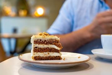 Piece of carrot cake on table in coffee shop with man in background during break