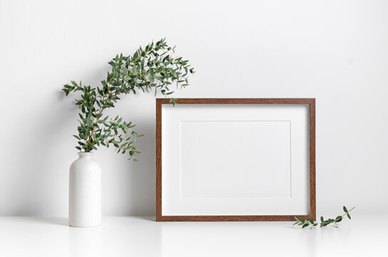Blank picture frame mockup in scandinavian style over white wall with green eucalyptus in vase
