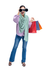 Asian Muslim woman in a headscarf looking through binoculars while holding shopping bags