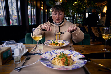 Pretty mature woman eating seafood spaghetti at restaurant table