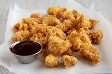 Homemade Popcorn Chicken with BBQ Sauce on a white wooden background, side view.